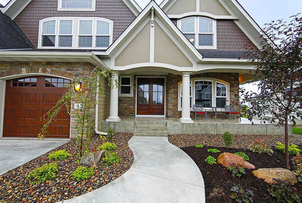 House plan exterior featuring a covered porch with columns, stone facade, double front doors, and arched windows.