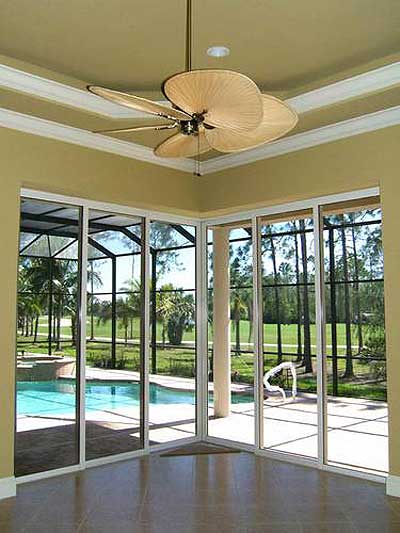 Interior view of a sunroom with sliding glass doors opening to a screened pool area and golf course view.