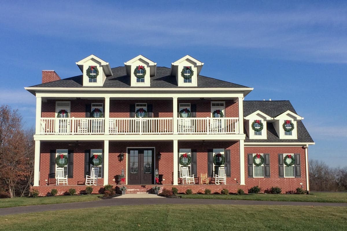 House plan exterior. Two-story Colonial with a large front porch, dormers, and brick exterior with white trim. Features include a symmetrical design.