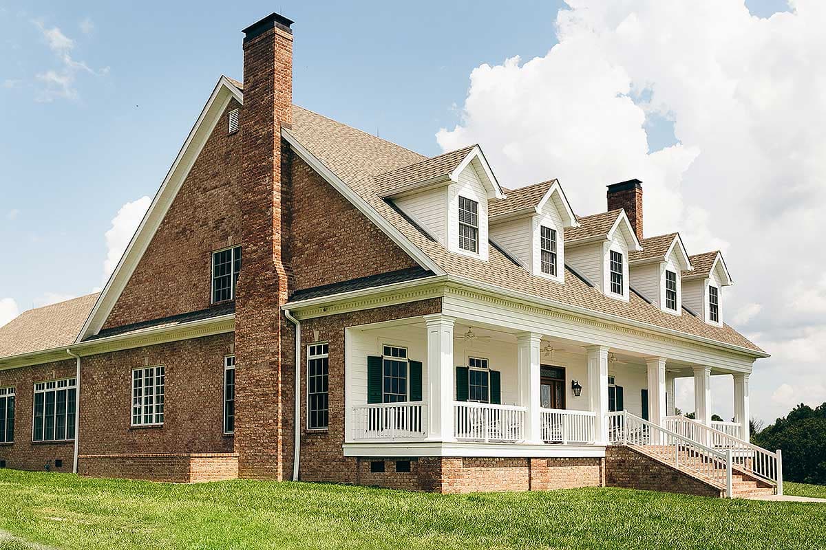 House plan exterior: Brick and siding two-story home with a full-width wrap-around porch, dormers, and a prominent brick chimney.