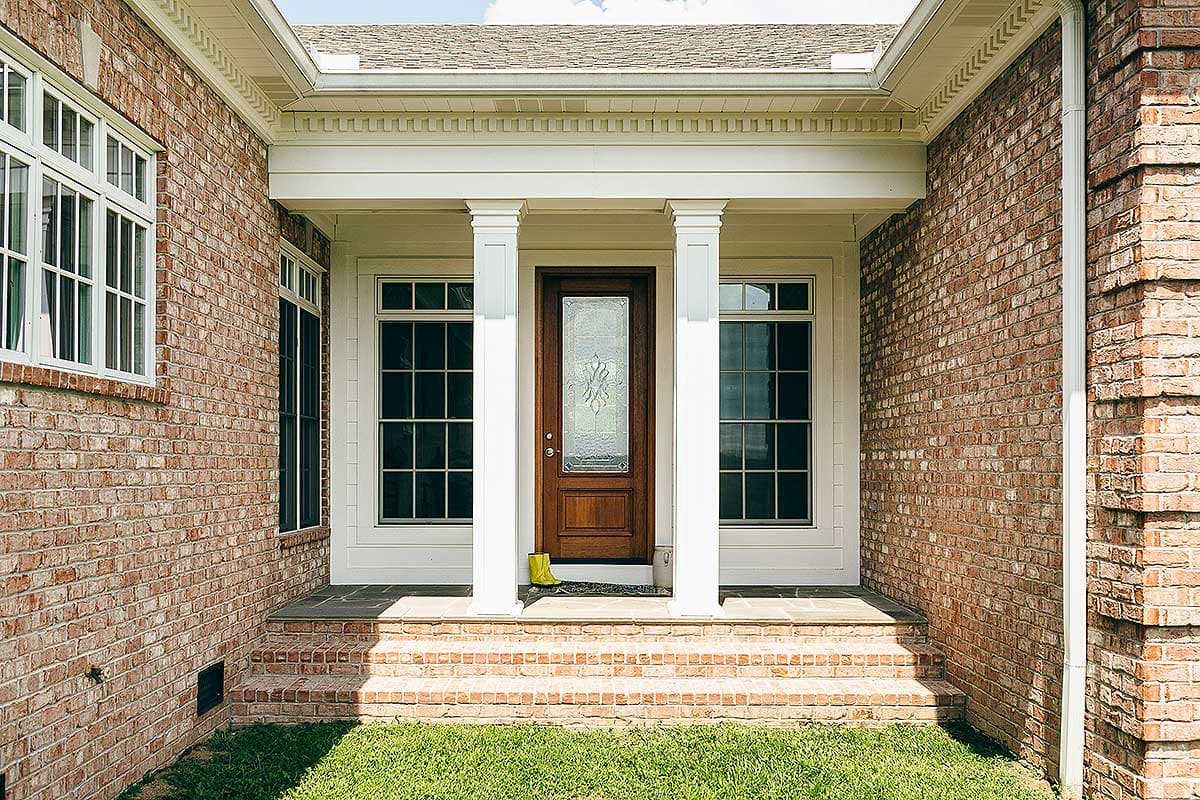 House plan exterior: brick facade with a covered entryway, central glass-paneled door, and flanking windows.