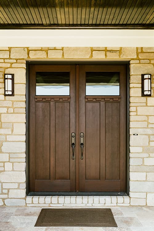House plan exterior with double wood doors, stone facade, and lantern sconces flanking the entrance.