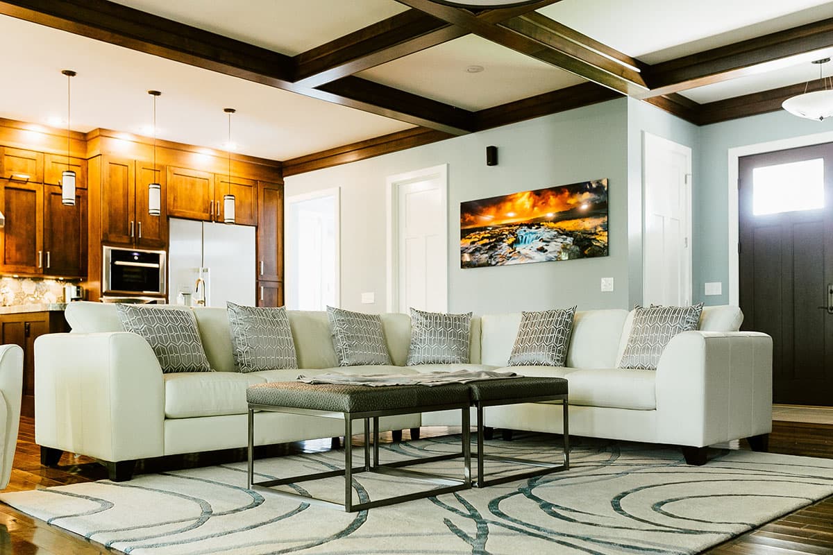 Living room with white sectional sofa, coffered ceiling, dark wood cabinetry, and entryway.