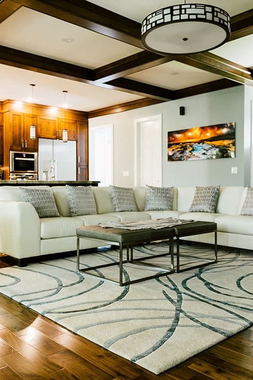 Living room with sectional sofa, coffered ceiling, dark wood cabinetry, and geometric pendant light.