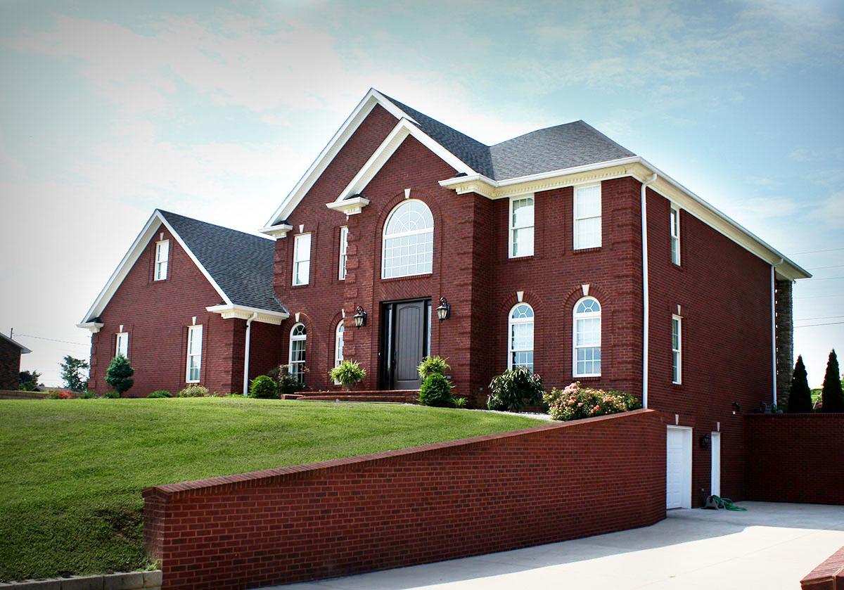 House plan exterior: Two-story brick home with a prominent arched window above the front door, multiple gables, and an attached garage.