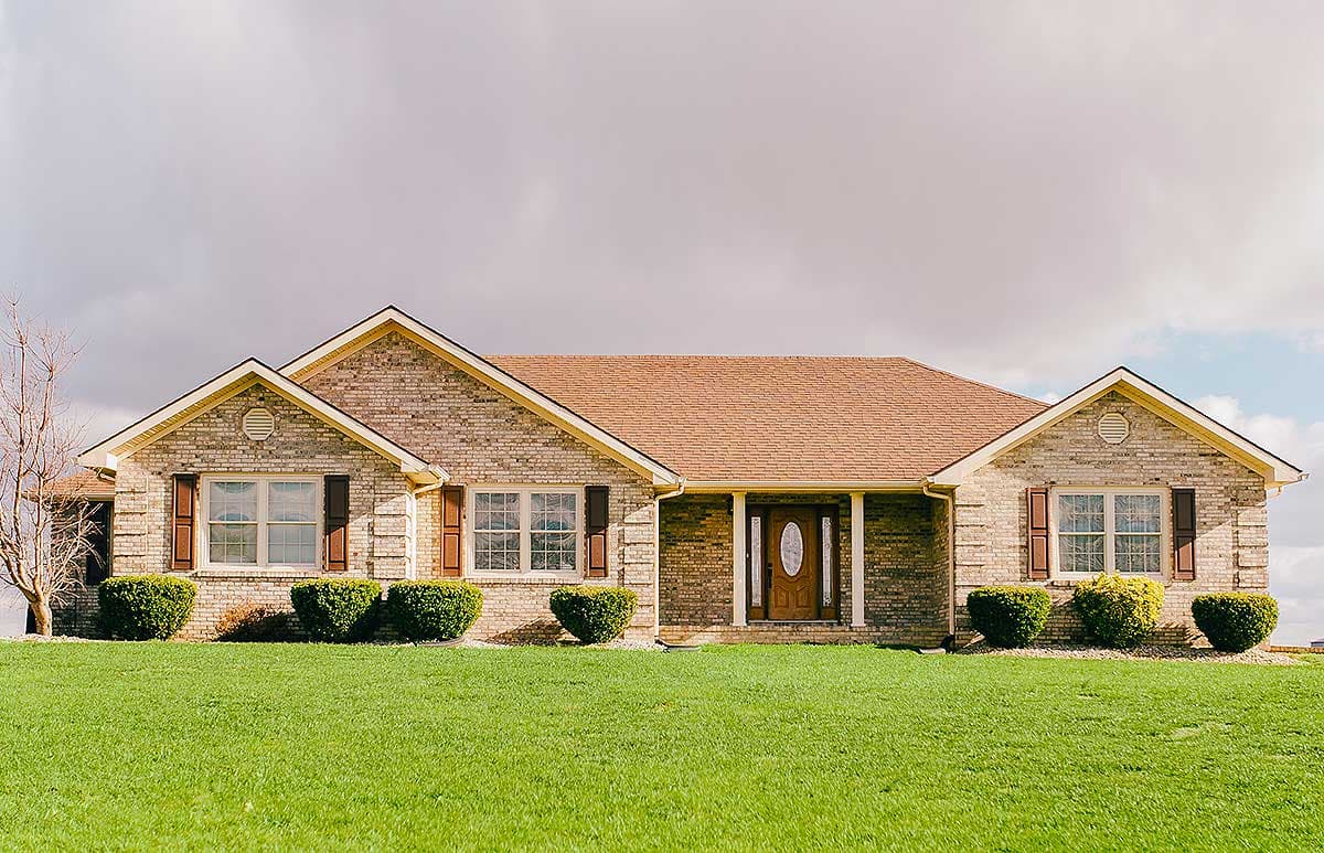 House plan exterior. Single-story Ranch home with brick facade, gable roof, and covered porch. Features include shutters and arched door detail.