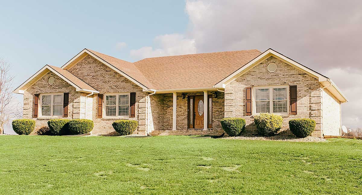 Ranch house plan exterior with brick facade, gabled roof, covered front porch with columns, and multiple dormers.