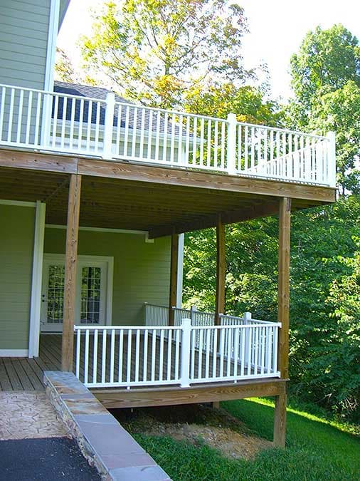 Two-level wooden deck with white railings. Lower level covers a covered porch with double doors.