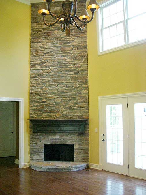 Great room with vaulted ceiling, floor-to-ceiling stacked stone fireplace, and double doors.