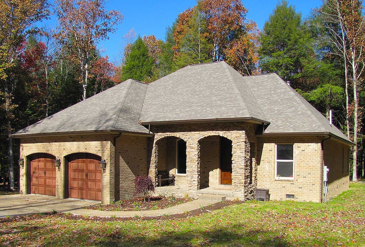 House plan exterior featuring brick facade, arched stone entry, and two-car garage with wood doors.