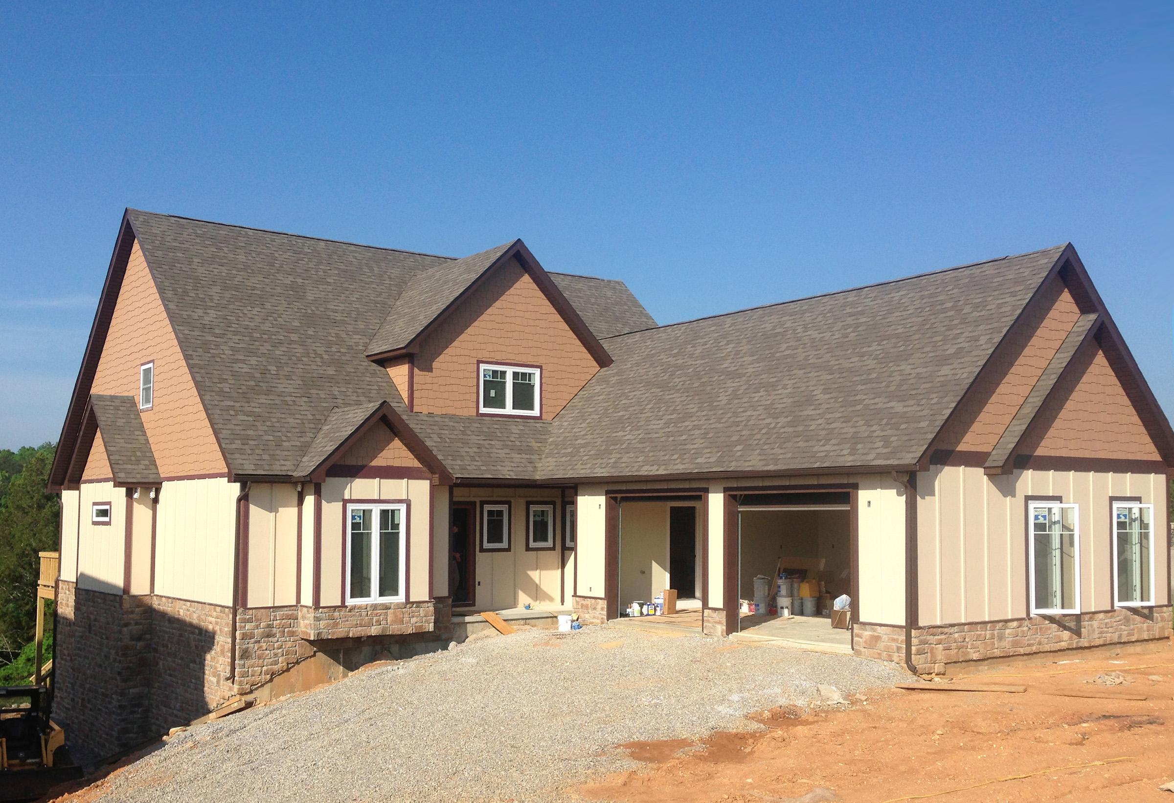 House plan exterior with mixed siding, stone accents, prominent gables, and a three-car garage under construction.