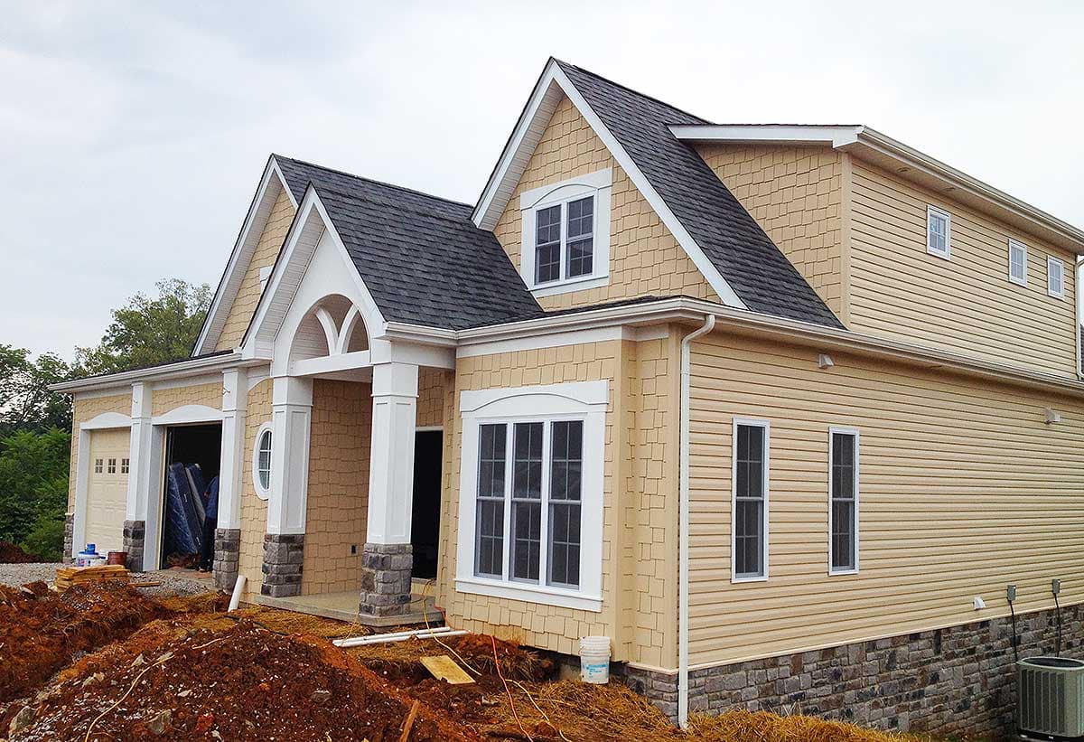 House plan exterior: Two-story home with attached garage, arched entryway, gable dormer, and shingle siding.