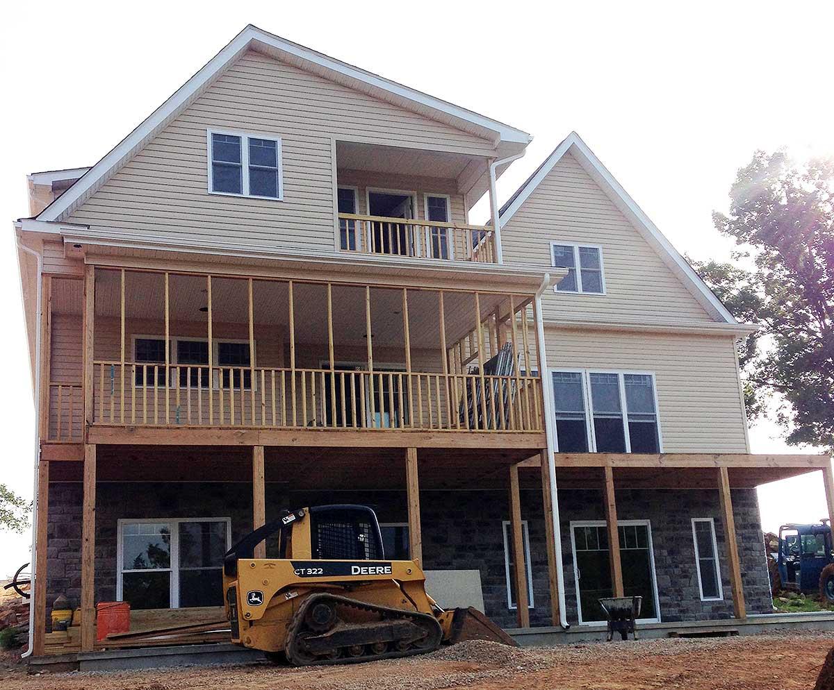 House plan exterior with two stories, screened porch, upper balcony, gabled roof, and stone foundation.