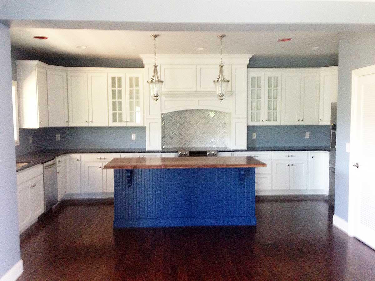 Kitchen featuring white cabinetry, a blue island with butcher block top, dark countertops, and glass tile backsplash.
