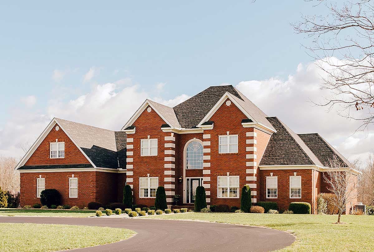 Two-story brick house plan with symmetrical gables, arched entryway, and decorative quoins.