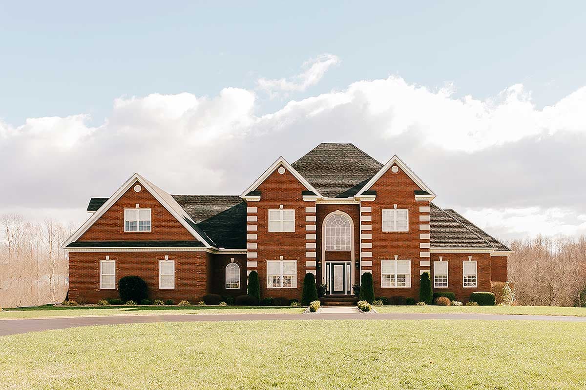 House plan exterior view of a two-story brick home with a central arched window, multiple gables, and a side-facing garage.