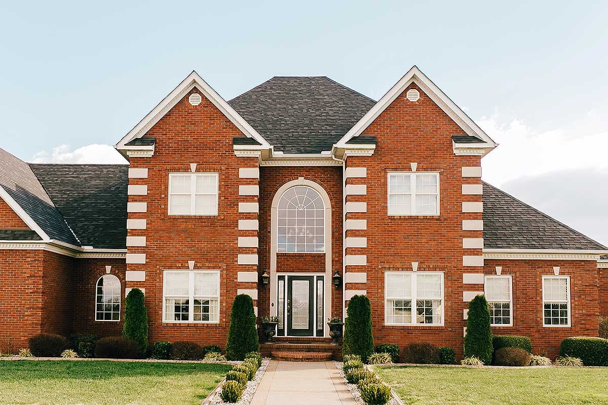 House plan exterior: Two-story brick home with a central arched entryway, symmetrical gables, and white trim.
