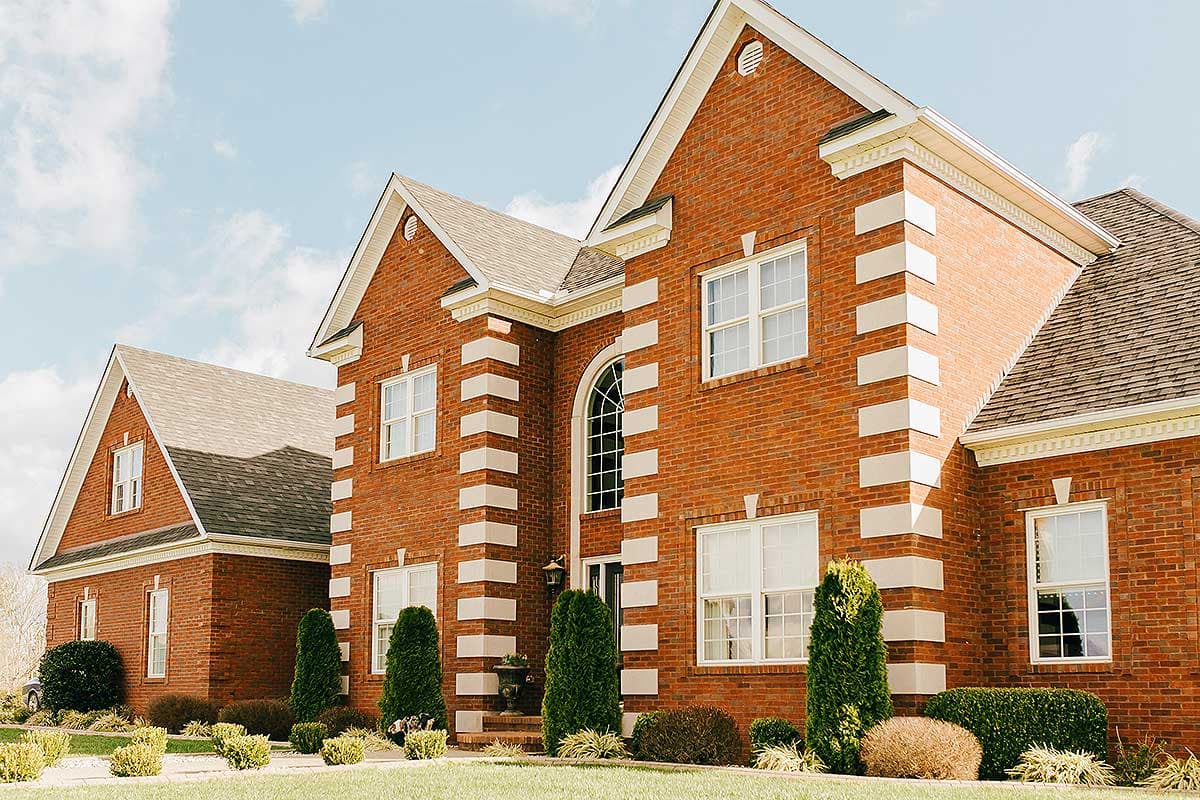 Two-story brick house plan exterior with white quoins, gables, and an arched window above the entrance.