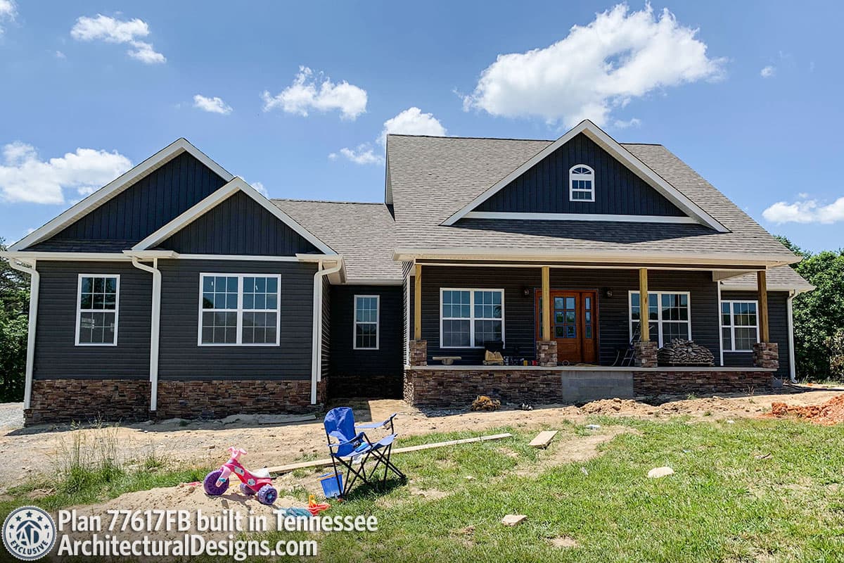 House plan exterior: Ranch style, single-story home with dark siding, stone accents, and a covered front porch with wooden posts.