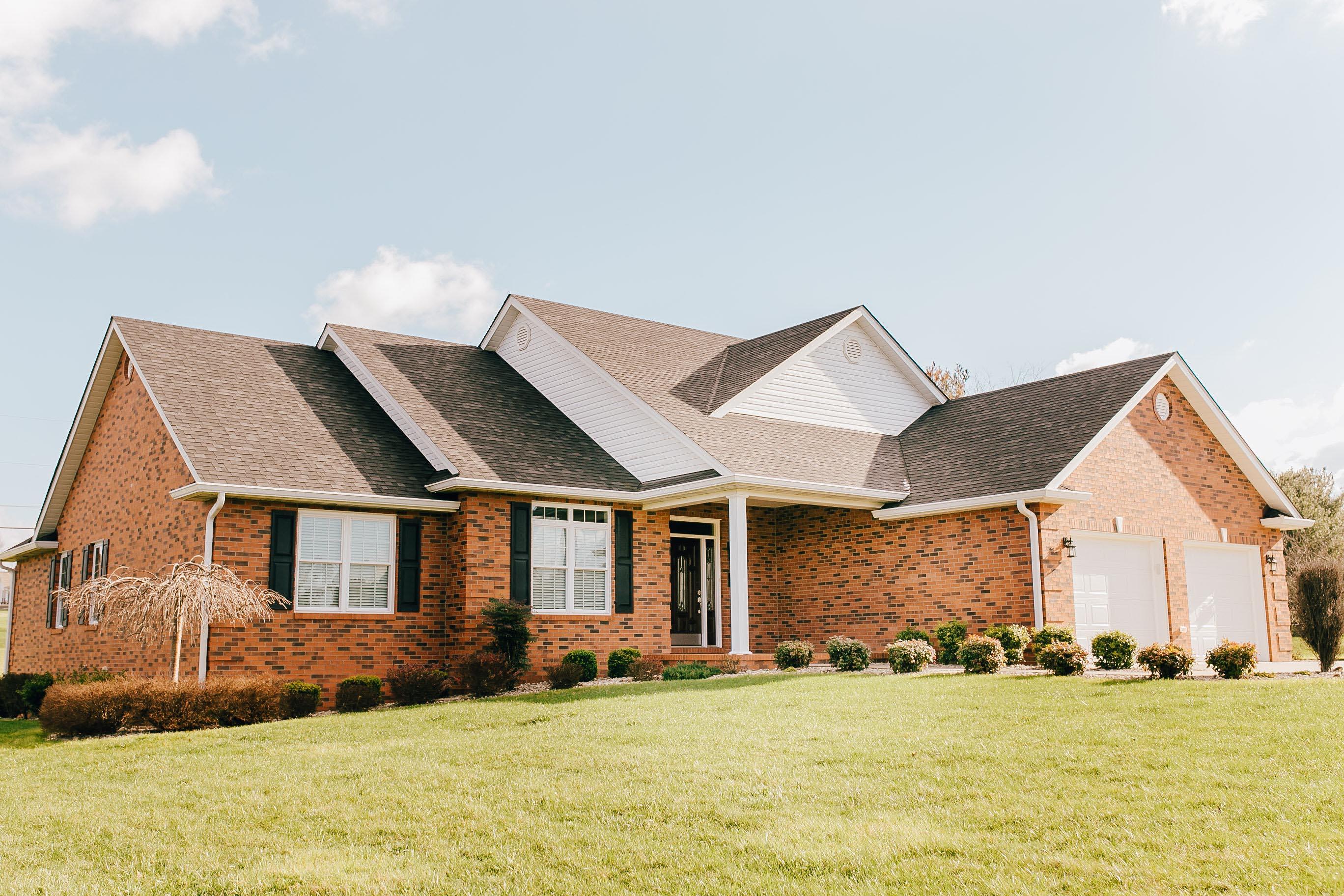Ranch-style brick house plan exterior with a covered front porch, multiple gables, and a three-car side-entry garage.