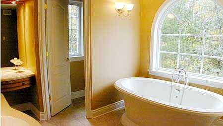Freestanding tub with arched window, vanity, and doorway to a separate room with a window.