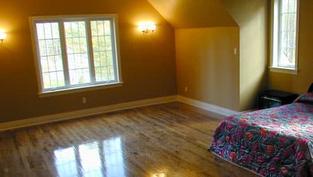 Bedroom interior with wood floors, sloped ceiling, large multi-pane window, and bed.