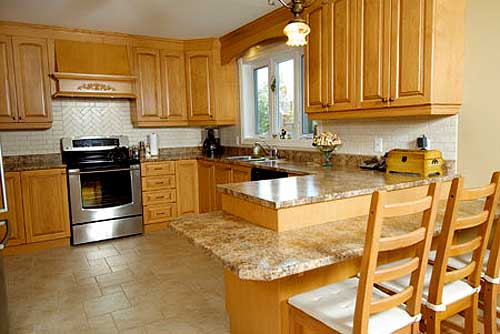 Kitchen with light wood cabinets, granite countertops, stainless steel range, island with seating, and herringbone tile backsplash.