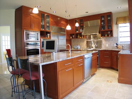 Kitchen featuring cherry wood cabinets, a large granite island with seating, stainless steel appliances, and a mosaic tile backsplash.
