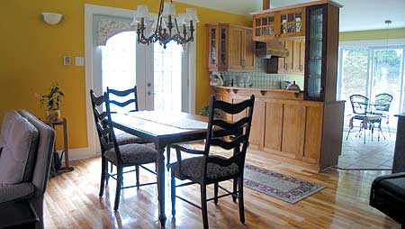 Dining area with wooden table and chairs adjacent to a kitchen with natural wood cabinetry and a peninsula.