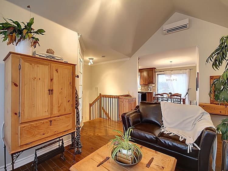 Interior view of living area with vaulted ceiling, a leather sofa, wooden cabinet, and view into dining room and kitchen.