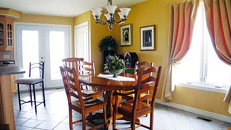 Dining room with wooden table and chairs, French doors, and window with pink drapes.