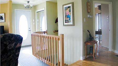 Interior view of a house entrance hall with a white oval-windowed front door, wooden staircase railing, and artwork on the wall.