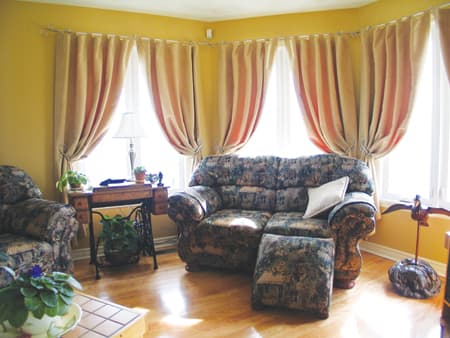 Living room interior with two upholstered armchairs and a sofa with ottoman in front of bay windows.