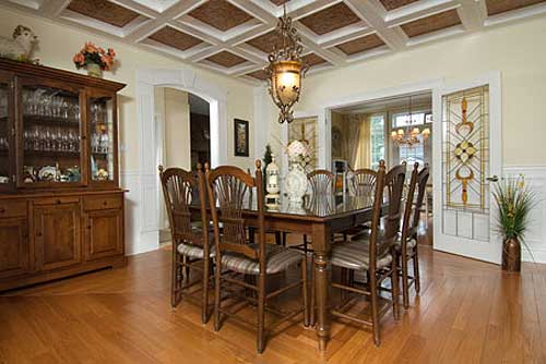 Dining room with wood hutch, table and chairs, coffered ceiling, and stained glass door.
