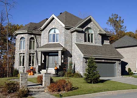 House plan exterior: Two-story home with stone facade, prominent gables, arched windows, covered entry, and attached two-car garage.