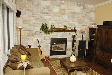 Living room with stone fireplace, mantel, sofa, coffee table, and wood entertainment center.
