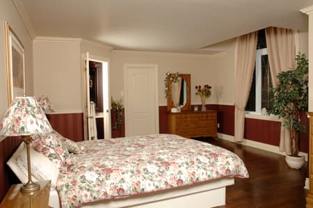Interior view of a bedroom featuring a king-size bed, dresser with mirror, and access to a closet. Wood flooring.