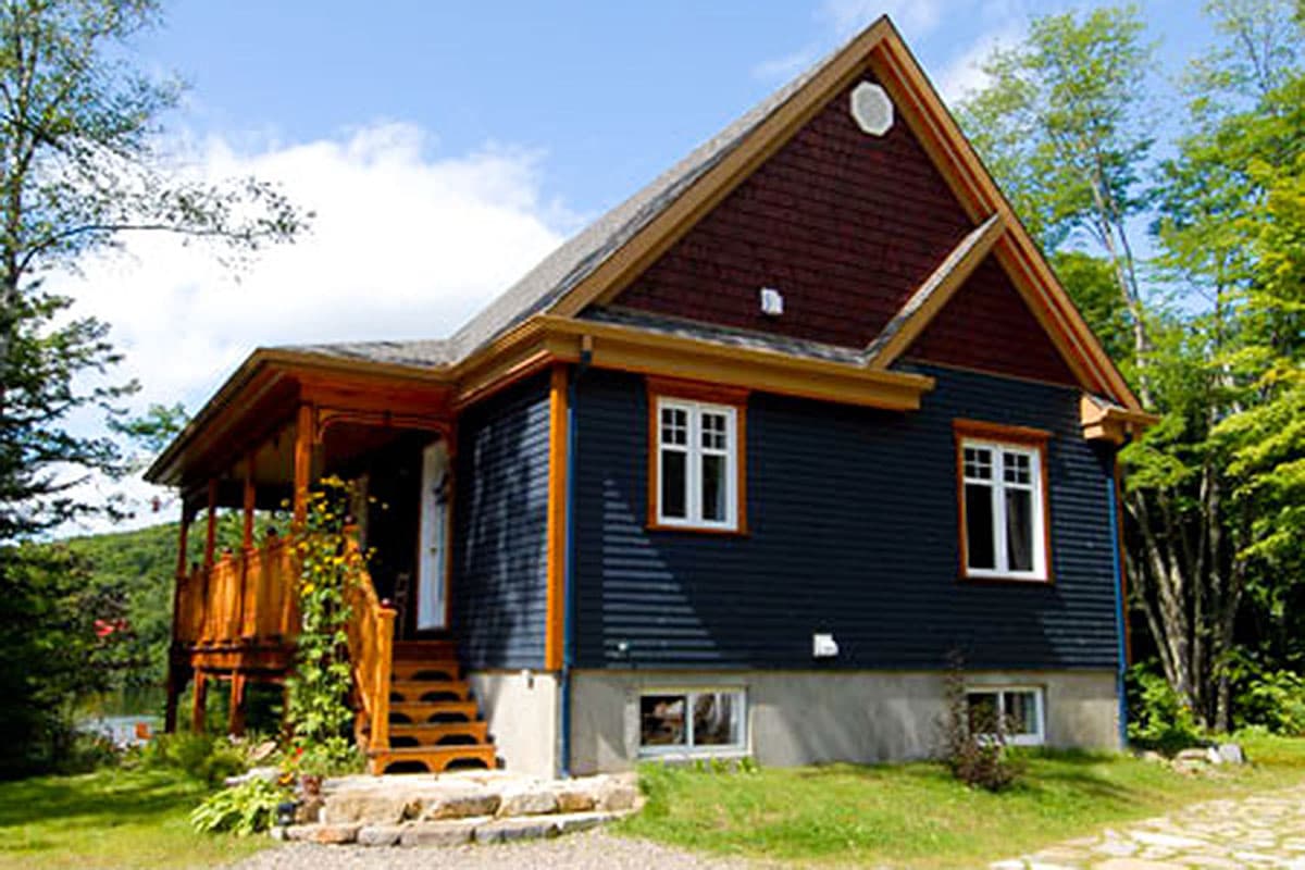 House plan exterior: Dark blue sided two-story house with a large wooden porch, gabled dormer and cedar shingles on gable.