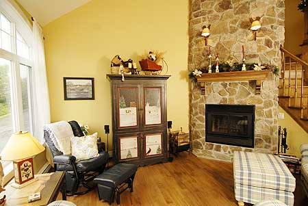 Living room with a large stone fireplace, vaulted ceiling, and tall windows.
