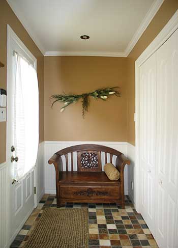 Entryway with paneled walls, a wooden bench with carved details, and a patterned tile floor.
