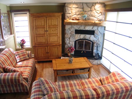 Living room with stone fireplace, wooden armoire, coffee table, and plaid sofas.