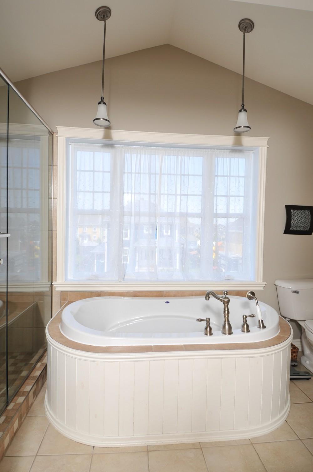 Bathroom with a corner soaking tub, glass-enclosed shower, and a window with sheer curtains.