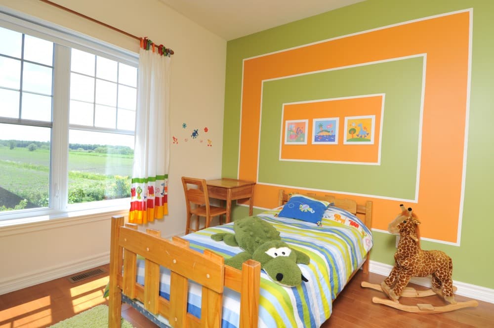 Children's bedroom with wood bed, desk, rocking giraffe, and accent wall with framed art.