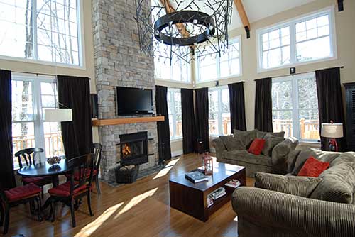 Great room with stone fireplace, vaulted ceiling with wood beams, and large windows.