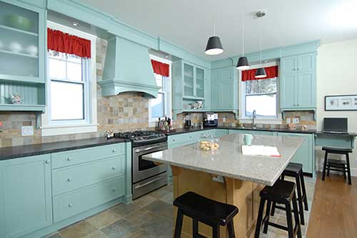 Corner kitchen with teal cabinetry, granite island, stainless steel range, and stone tile backsplash.
