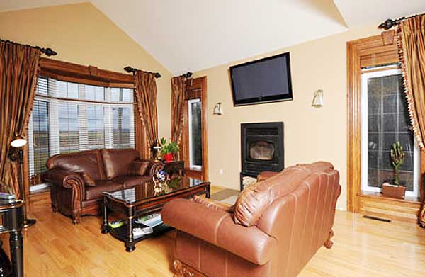 Living room interior with vaulted ceiling, fireplace, TV, bay window, and leather sofas.