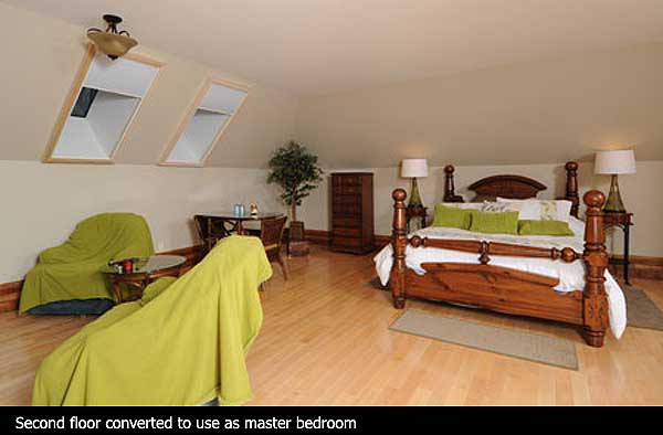Bedroom with sloped ceilings, two skylights, wooden furniture including a four-poster bed, and a seating area.