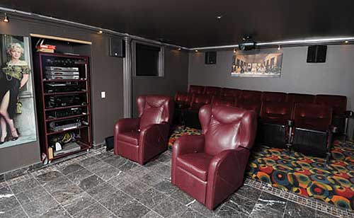 Home theater with tiered seating, plush chairs, media rack, and projection screen.