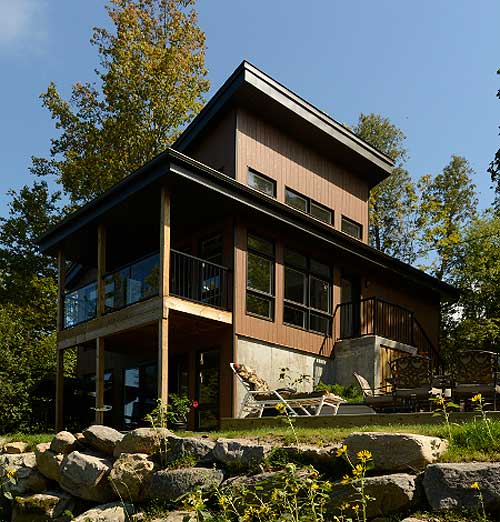 Modern house plan exterior with two stories, large windows, a covered deck with glass railings, and a sloped roof.