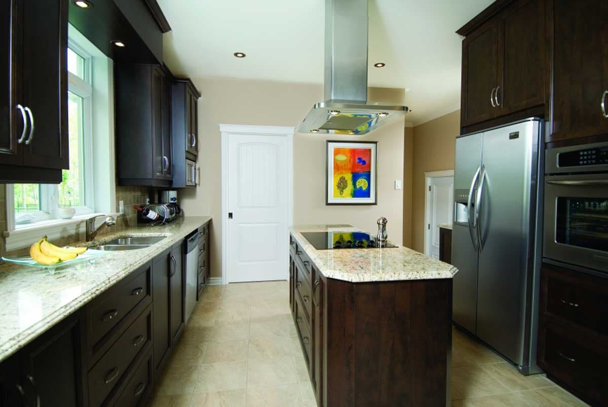 Kitchen interior with dark wood cabinets, granite countertops, island with cooktop, stainless steel refrigerator, and range.